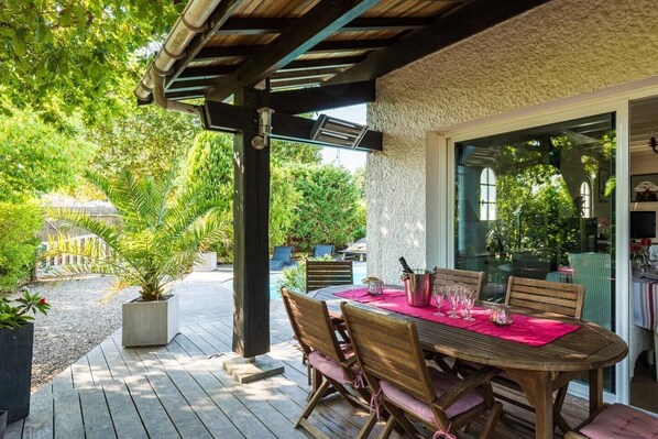Un patio techado con una mesa lista para comer, rodeado de sillas y vistas al jardín.