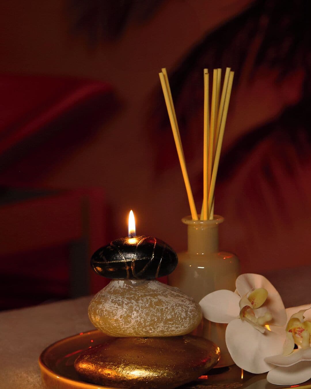 Uma vela, incensos, uma pedra e uma orquídea sobre uma mesa.