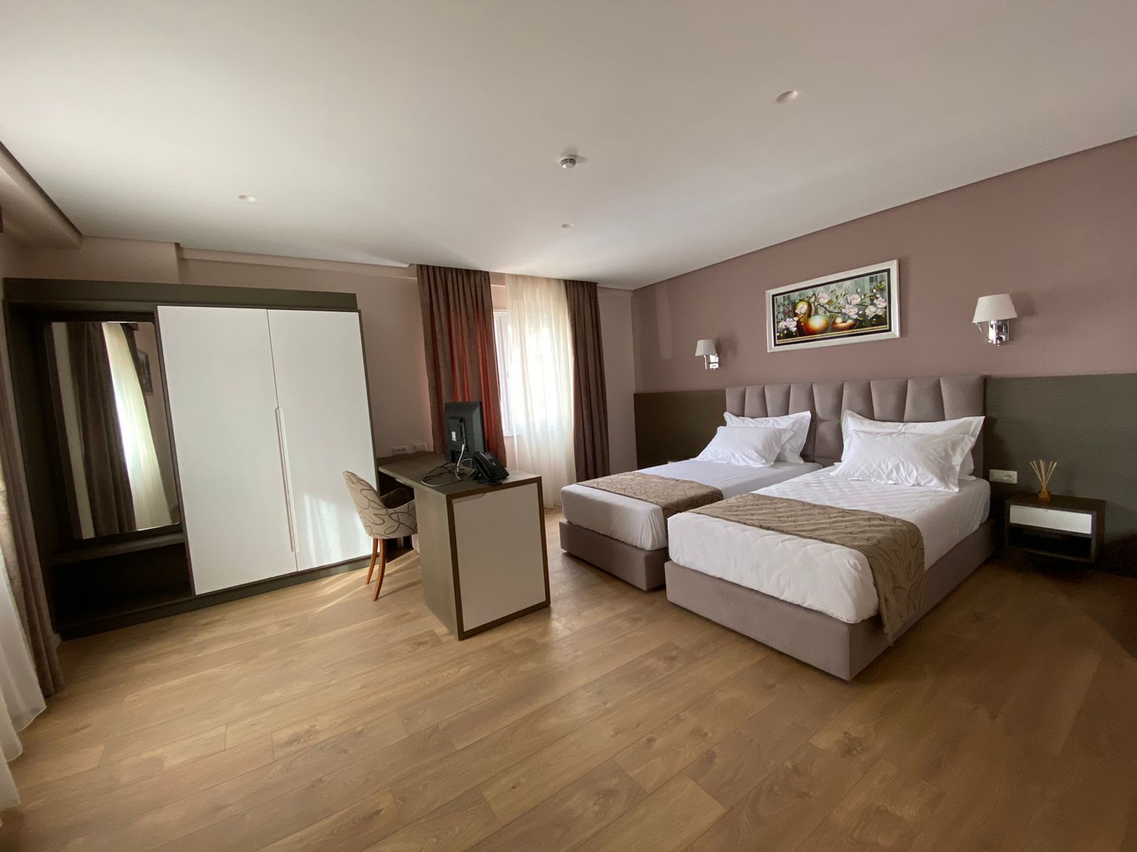 Ett hotellrum med två sängar, ett skrivbord, en stol, en garderob och en tavla på väggen.