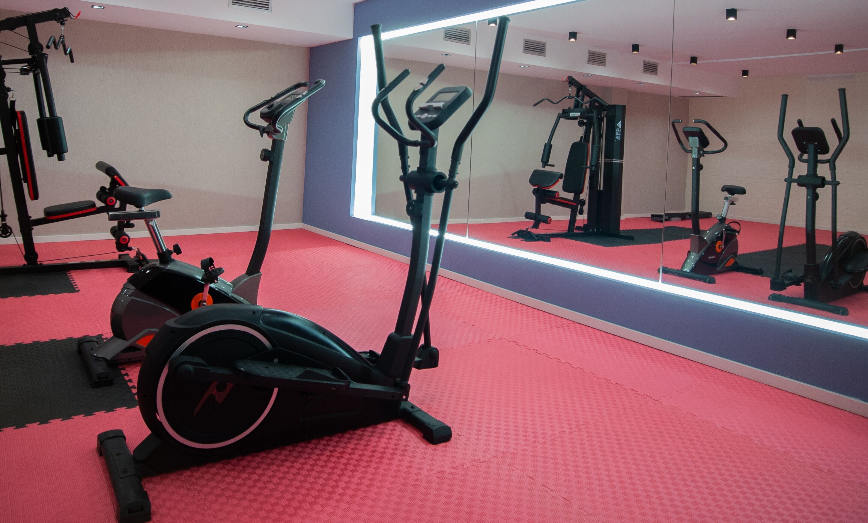 Un gimnasio con equipo de ejercicio, suelo rojo y un espejo grande.