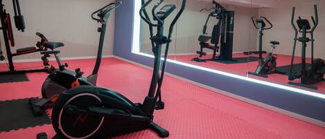 Un gimnasio con equipo de ejercicio, suelo rojo y un espejo grande.