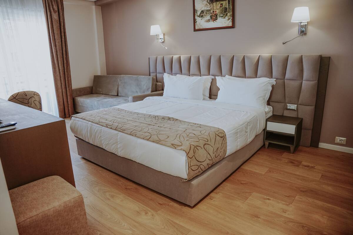 A hotel room with a large bed, a bedside table, a chair, and a desk.