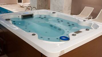 A hot tub with a control panel, two lounge chairs, and a pool in the background.