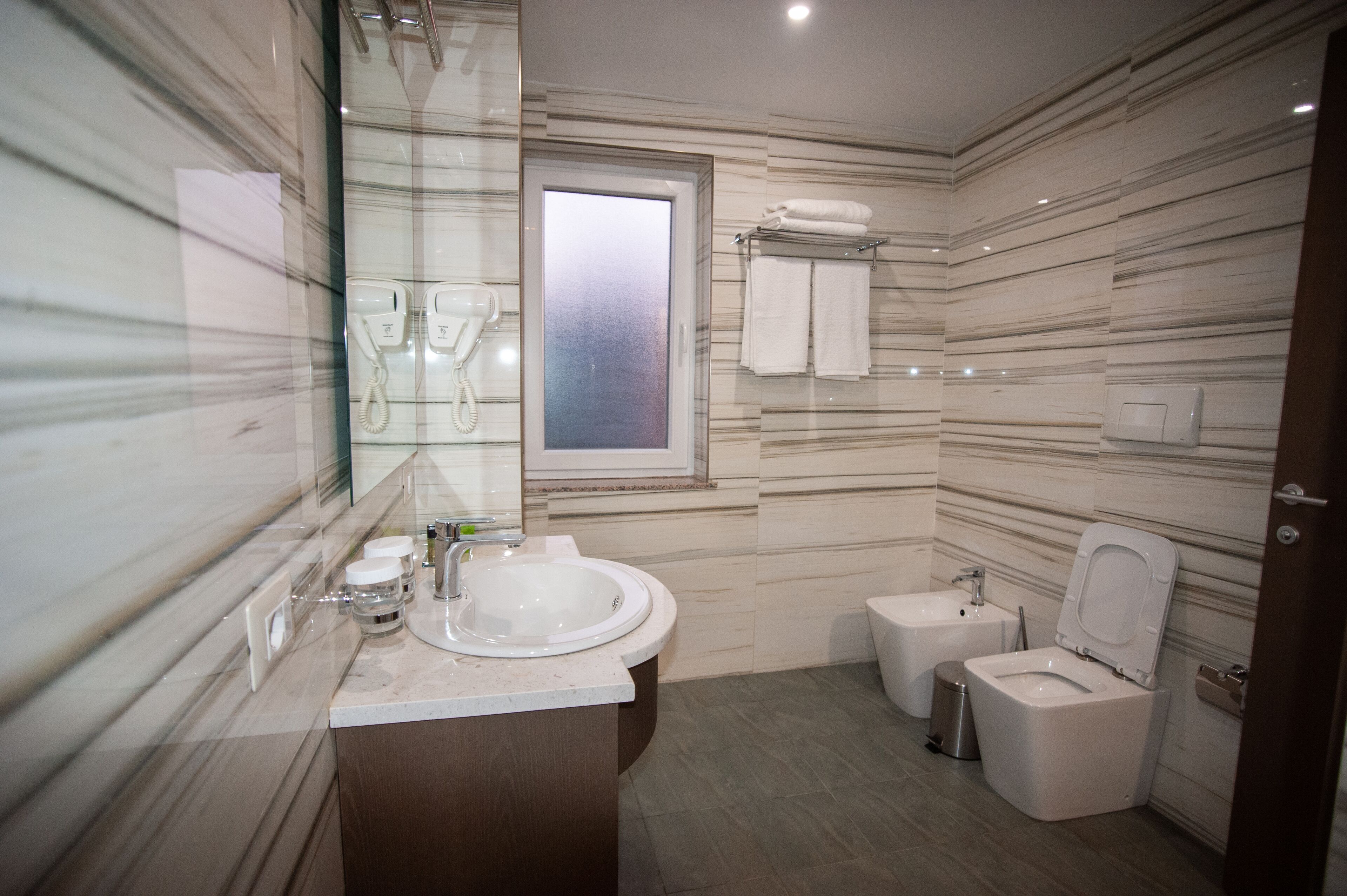 Un baño moderno con salpicadero de mármol, un lavabo, un inodoro y ducha con mampara de vidrio.