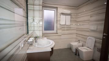 Un baño moderno con salpicadero de mármol, un lavabo, un inodoro y ducha con mampara de vidrio.