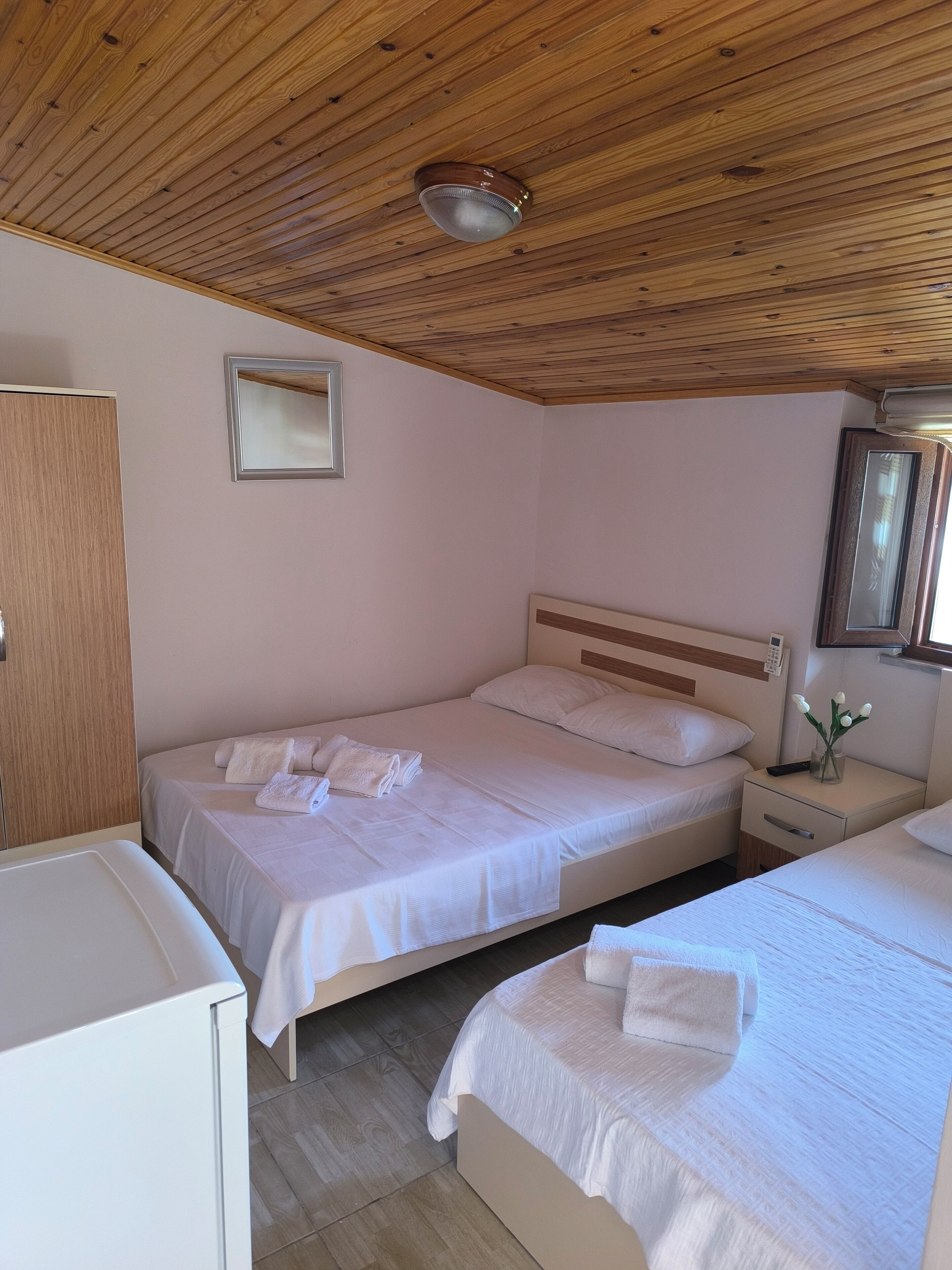 A bedroom with two beds, wooden ceiling, and a bedside table with a vase of flowers.