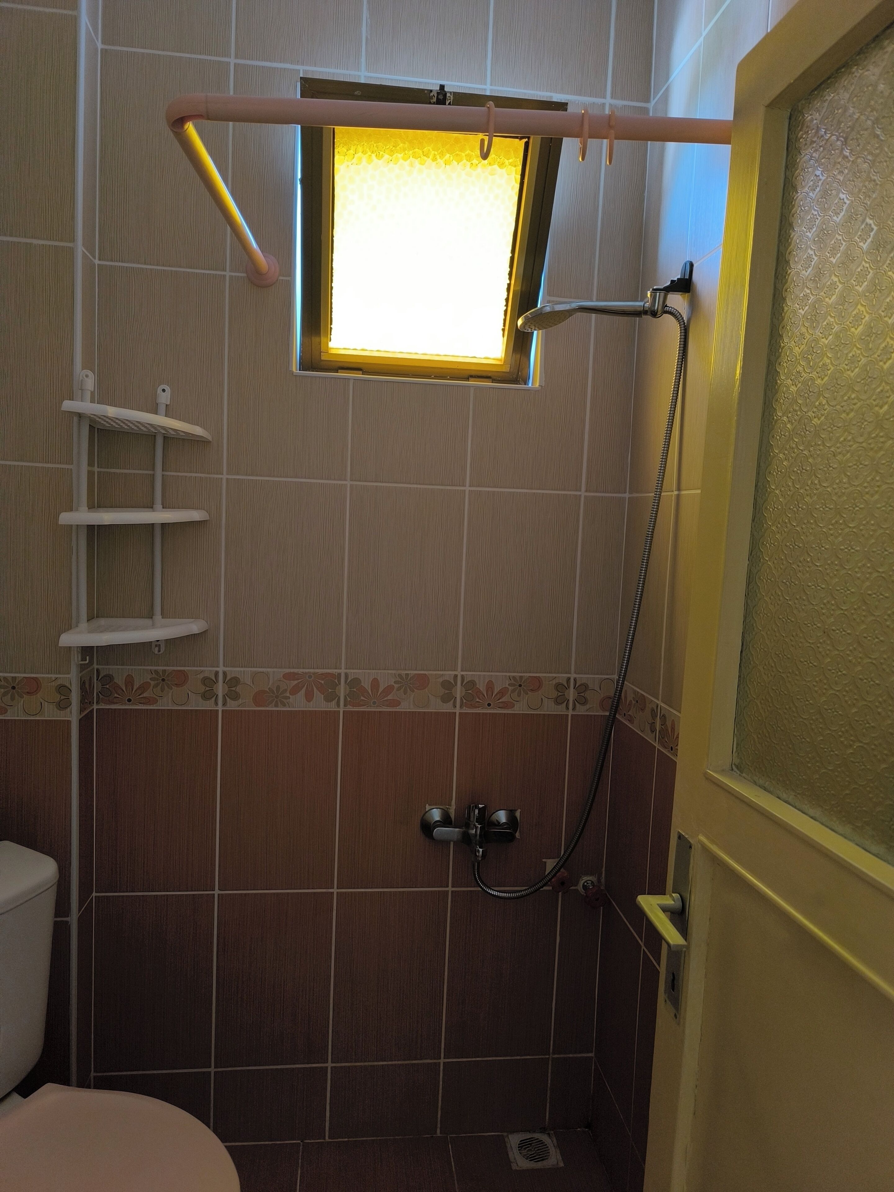 Une salle de bain avec une douche, des toilettes et une petite fenêtre.