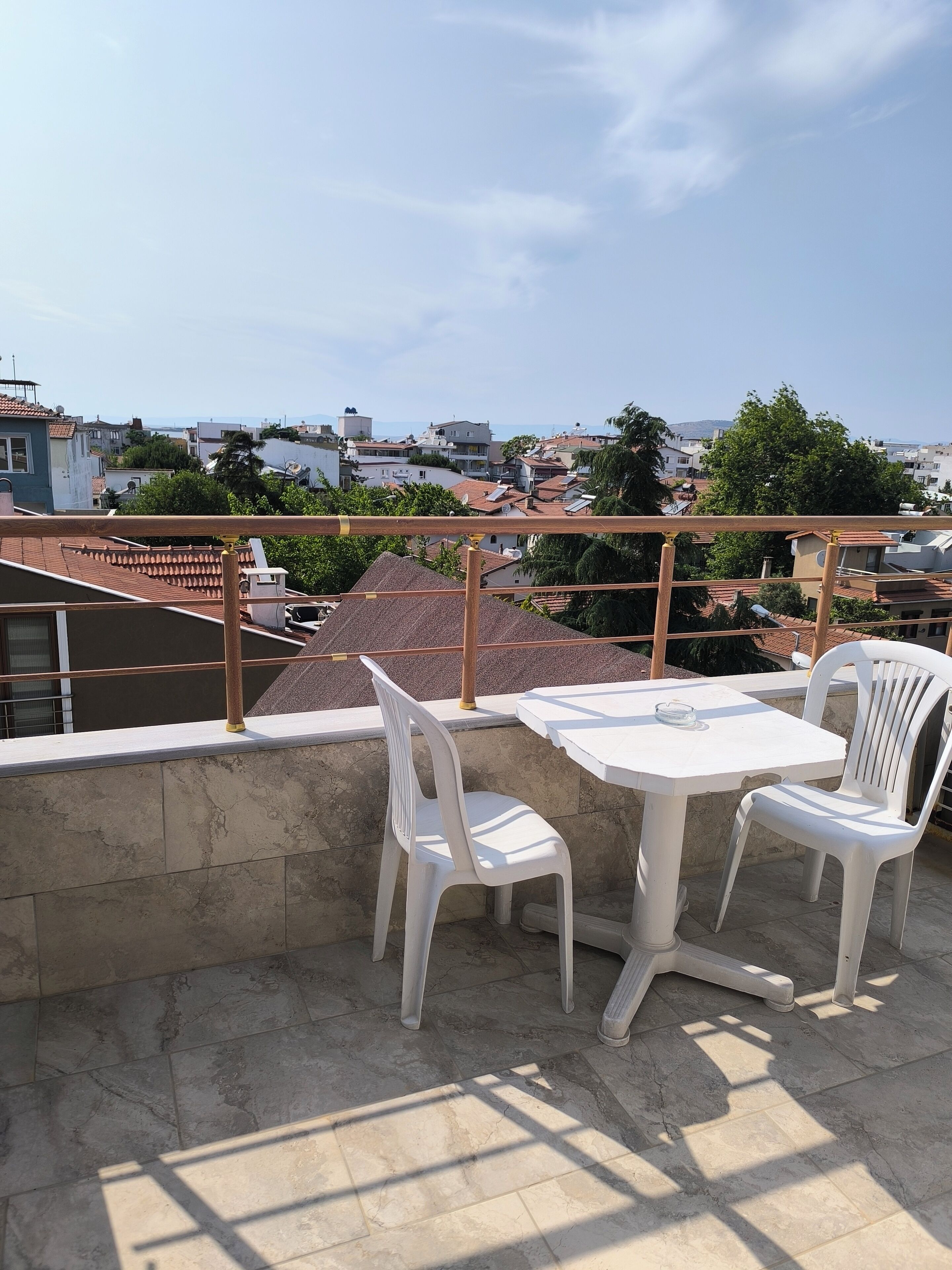 A terrace with a table and two chairs, overlooking a residential area with houses and trees.