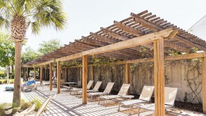 Une pergola en bois avec des fauteuils et un espace barbecue.