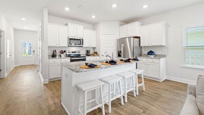 Une cuisine moderne avec des meubles blancs, des appareils en acier inoxydable et un îlot central doté de tabourets de bar.