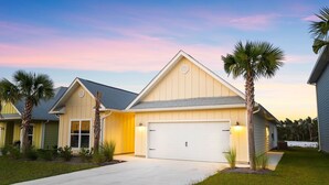 Une maison de plain-pied avec un garage, entourée de palmiers et d’une pelouse bien entretenue.