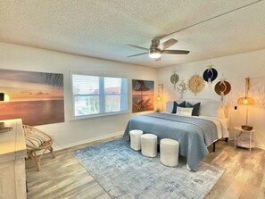 A bedroom with a bed, a ceiling fan, a window with blinds, and wall art. - Beachfront with heated pool, 60 seconds to beach (Cocoa Beach)