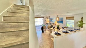 A spacious living area with a staircase, a dining table with chairs, a kitchen area, and a large window with a view. - Beachfront with heated pool, 60 seconds to beach (Cocoa Beach)