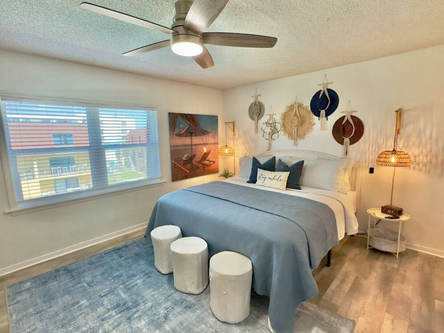 A bedroom with a bed, a ceiling fan, a window with blinds, and a painting on the wall.