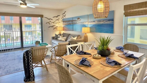 A dining area with a wooden table, white chairs, and a hanging light fixture. - Beachfront with heated pool, 60 seconds to beach (Cocoa Beach)