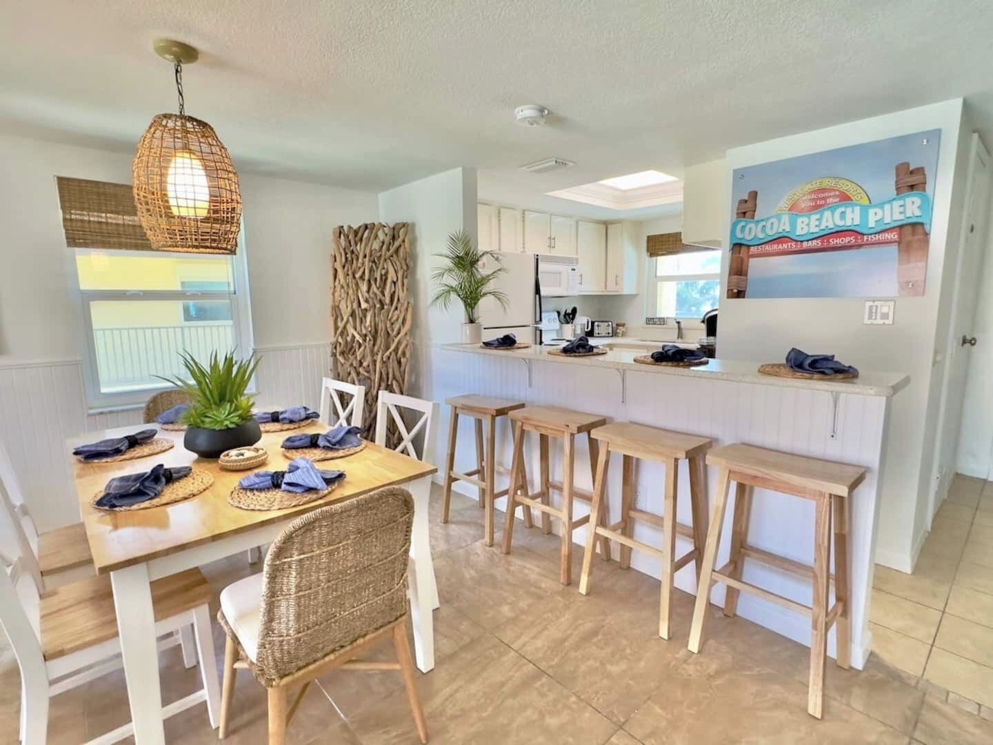 A modern kitchen with white cabinets, a central island with stools, and a dining area with wicker chairs and a table set for four.