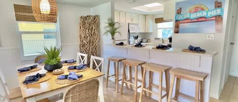 A modern kitchen with white cabinets, a central island with stools, and a dining area with wicker chairs and a table set for four.