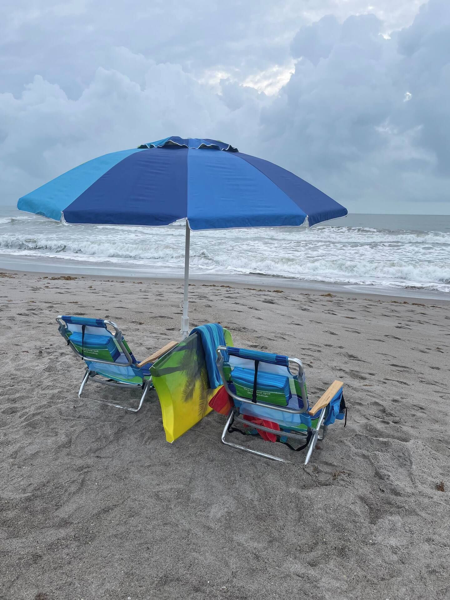 A beach with two beach chairs and a blue umbrella.