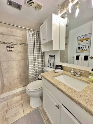 A modern bathroom with a shower, toilet, vanity, and a large mirror. - Beachfront with heated pool, 60 seconds to beach (Cocoa Beach)