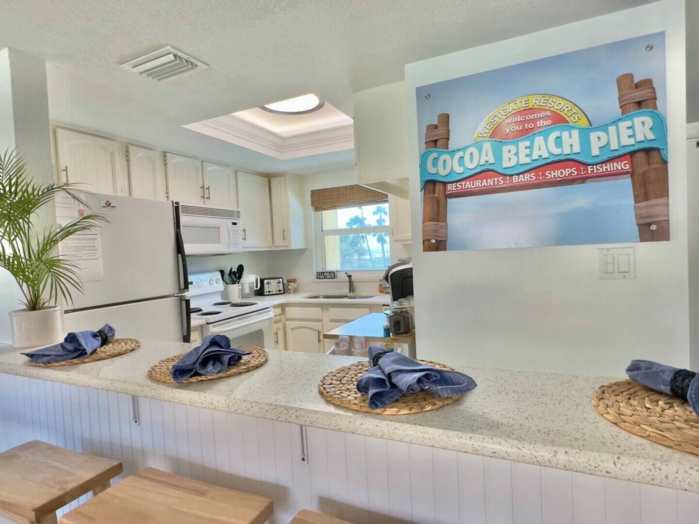 A kitchen with white cabinets, a microwave, and a stove. There is a sign on the wall advertising Cocoa Beach Pier.