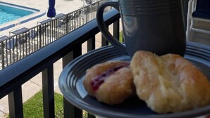 A balcony with a pool view, a plate of pastries, and a mug. - Beachfront with heated pool, 60 seconds to beach (Cocoa Beach)
