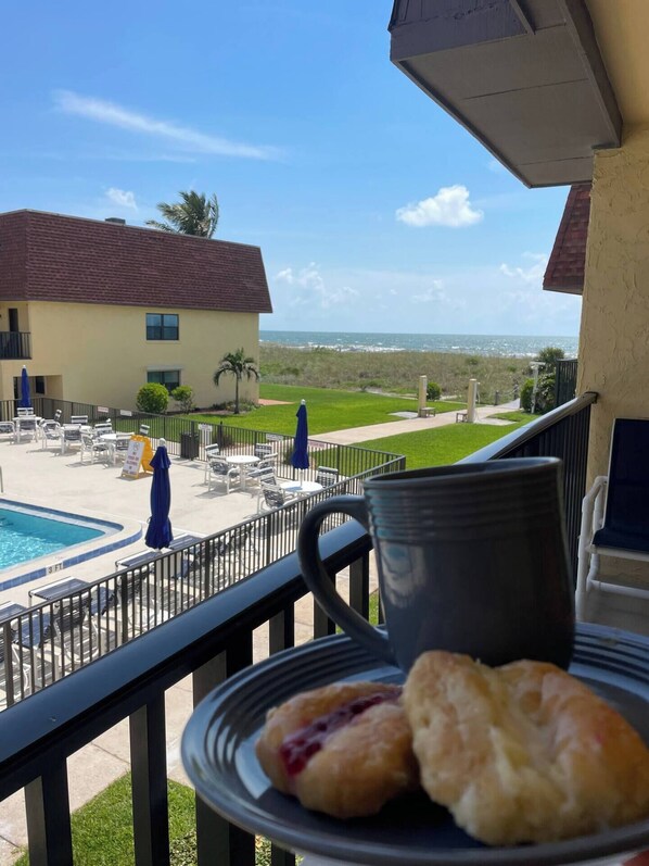 A balcony with a pool view, a plate of pastries, and a mug. - Beachfront with heated pool, 60 seconds to beach (Cocoa Beach)