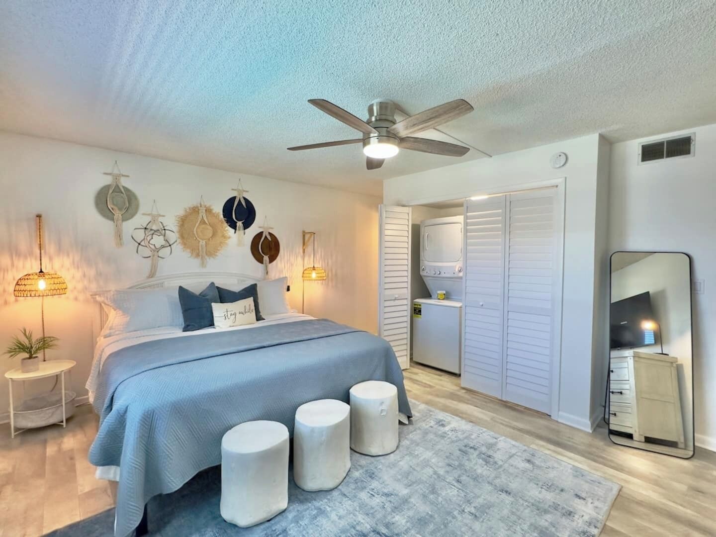 A bedroom with a bed, bedside lamps, a ceiling fan, a wardrobe, and a mirror.