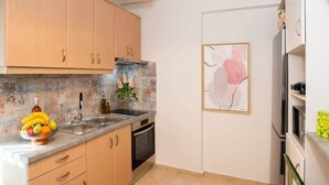 Eine Küche mit hellen Holzschränken, einer Edelstahlspüle, einer Mikrowelle und einem Herd. Auf der Arbeitsplatte steht eine Obstschale und an der Wand hängt ein gerahmtes Kunstwerk.