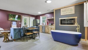 A modern kitchen with a large blue bathtub, a dining area with a table and chairs, and a mounted television displaying a waterfall scene. - Gentle Breeze: The Maple: Romantic Secluded Getaway (Lancaster)