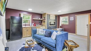A compact living space with a blue sofa, a black refrigerator, wooden cabinets, a kitchen area, and a door. - Gentle Breeze: The Maple: Romantic Secluded Getaway (Lancaster)