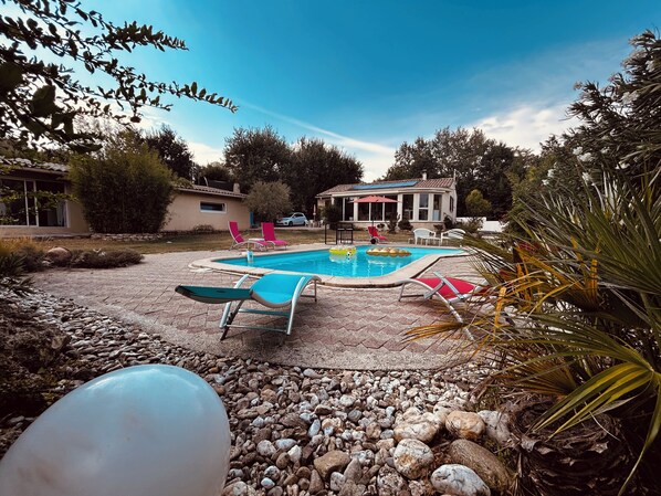 A backyard with a swimming pool, lounge chairs, and a house in the background.