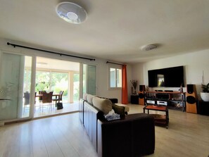 Ein modernes Wohnzimmer mit einer Couch, einem Couchtisch, einem Fernseher und einem Essbereich mit Stühlen und einem Tisch.