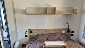 A bed with a quilted headboard, a bedside table, and a wall-mounted shelf.