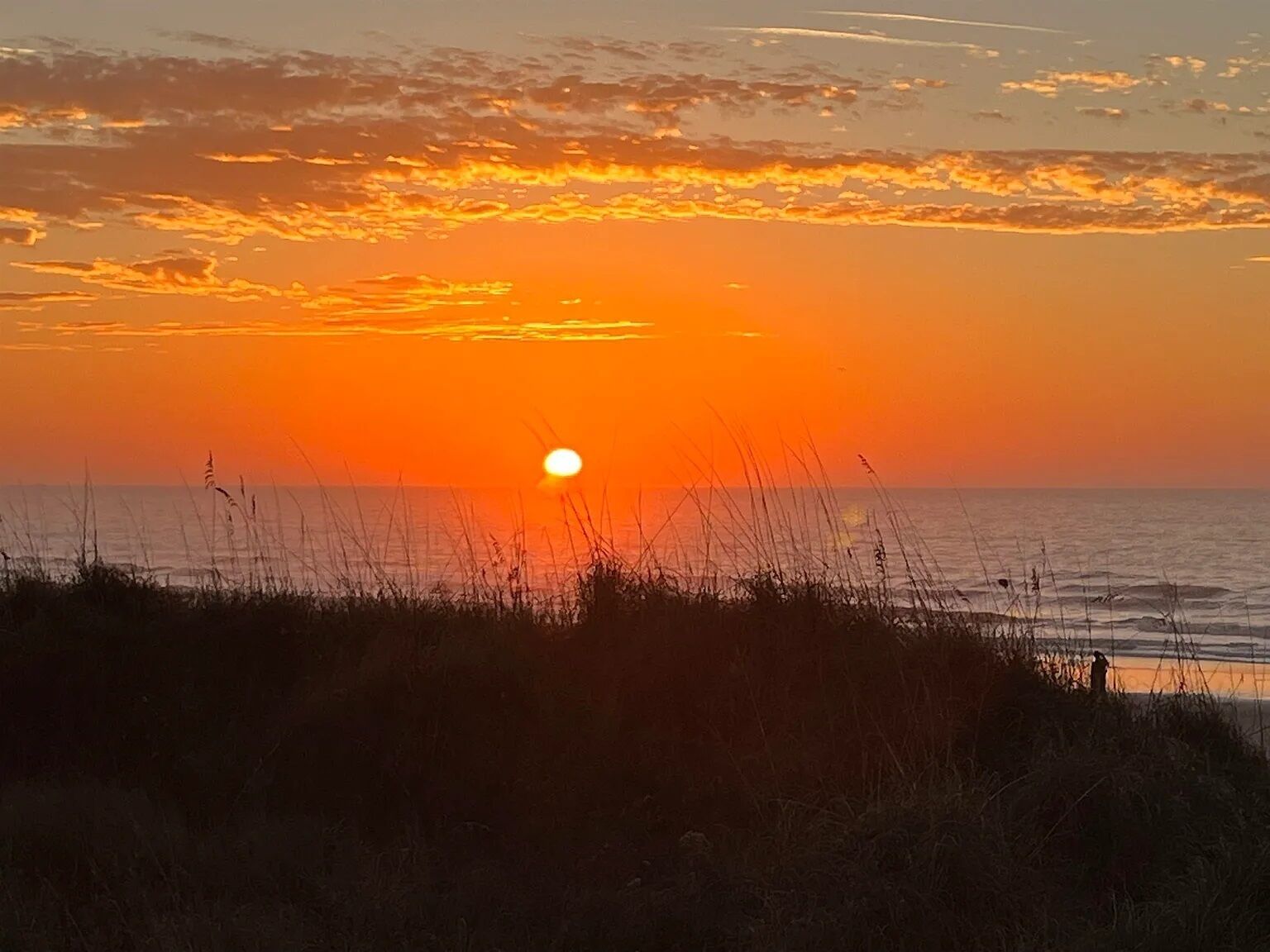 Een zonsondergang boven de oceaan, met een heldere lucht en geen zichtbare gebouwen of herkenningspunten.
