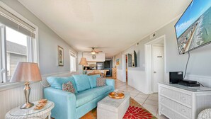 A living room with a blue sofa, a white coffee table, and a television mounted on the wall. - Direct Oceanfront, Cherry Grove, Elevator, 2 Bedroom Condo (North Myrtle Beach)