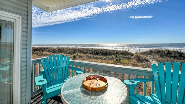 A balcony with two turquoise Adirondack chairs and a round glass table with a tray holding two wine glasses. The view includes a beach and ocean. - Direct Oceanfront, Cherry Grove, Elevator, 2 Bedroom Condo (North Myrtle Beach)