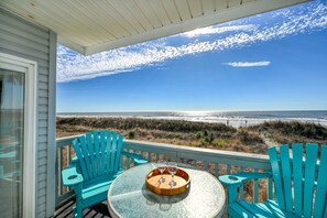 A balcony with two turquoise Adirondack chairs and a round glass table with a tray holding two wine glasses. The view includes a beach and ocean. - Direct Oceanfront, Cherry Grove, Elevator, 2 Bedroom Condo (North Myrtle Beach)