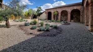Un patio con suelo de grava, un árbol y un edificio de ladrillo con arcos.