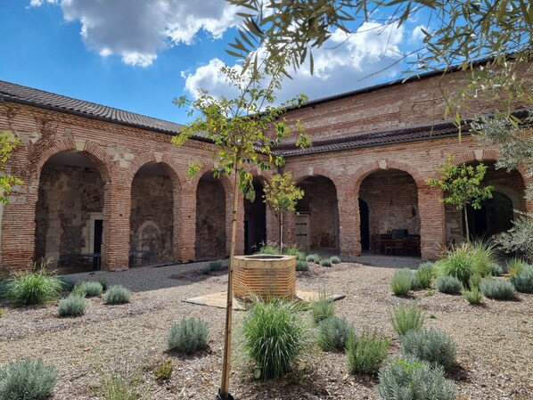 Un patio con arcos de ladrillo, un árbol central y vegetación circundante.