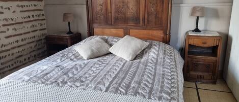 A bed with a wooden headboard, two pillows, and a patterned bedspread. There are two nightstands with lamps and a small wooden cabinet.