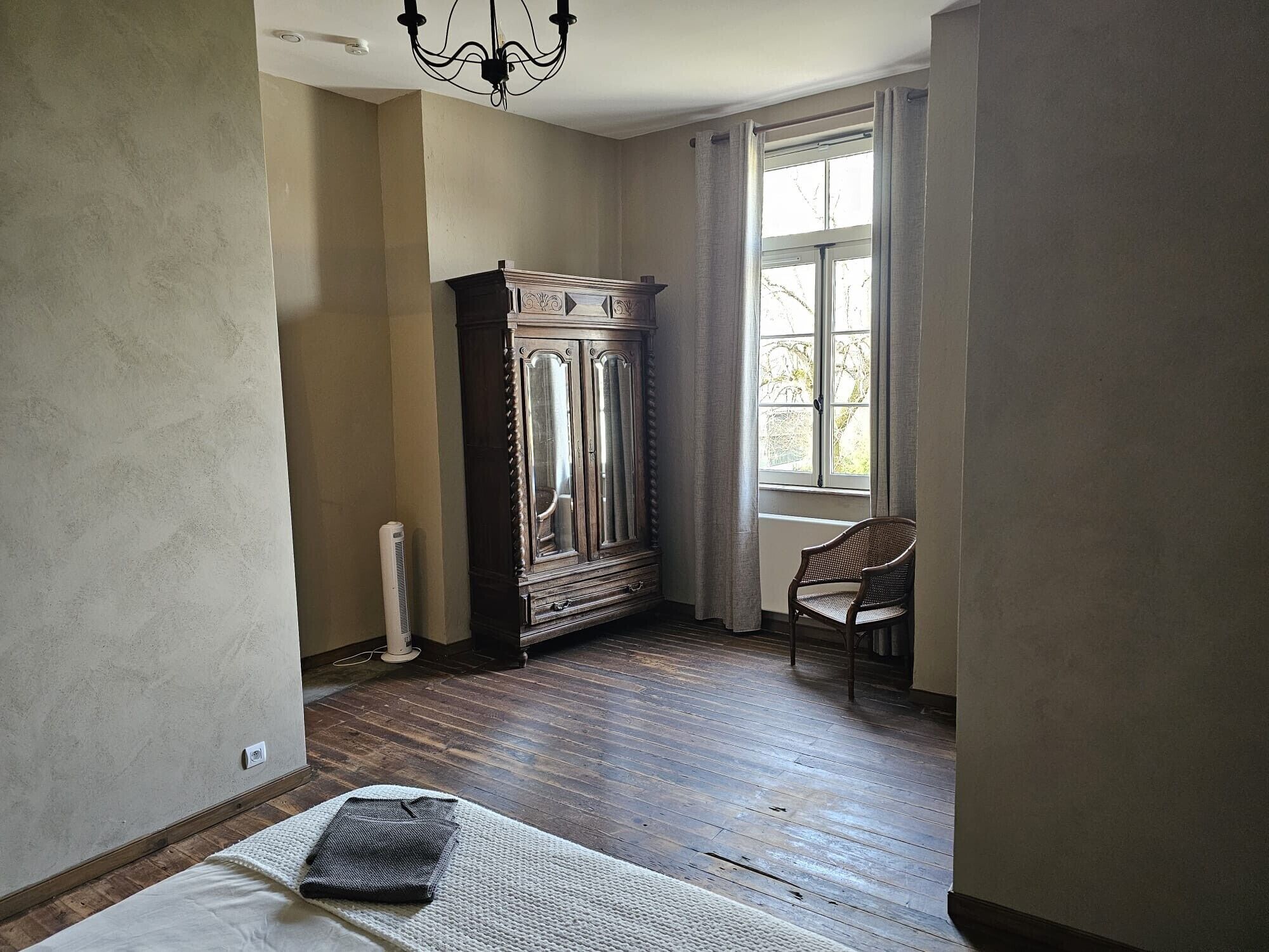 Une pièce comprenant un grand meuble en bois, une chaise et une fenêtre avec des rideaux.