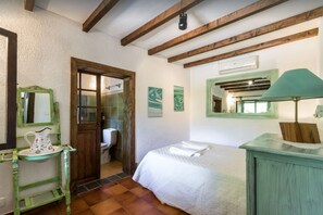 Un dormitorio con cama, puerta de madera, tocador verde, espejo y aire acondicionado de pared.