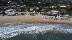 Vista aérea de una playa con una hilera de sombrillas y sillas de playa, arena y olas acercándose a la orilla.