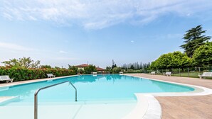 Une piscine entourée d’une terrasse carrelée, de bancs et de verdure, et dotée d’une rambarde de sécurité en métal.