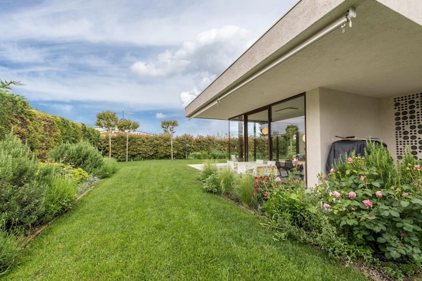 A modern house with a well-maintained lawn, a patio area, and a garden with various plants and flowers.