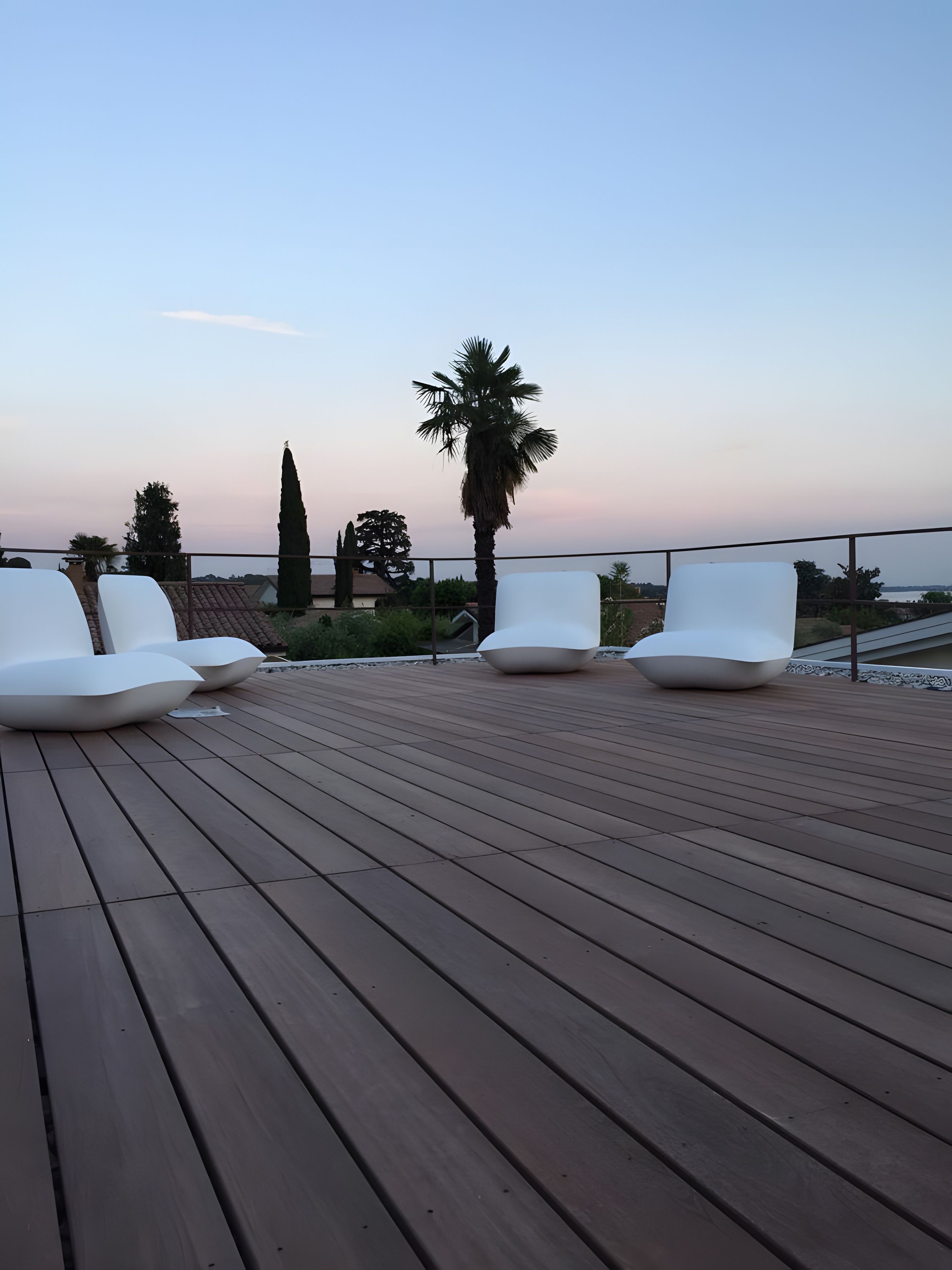 A wooden deck with white lounge chairs and a palm tree.