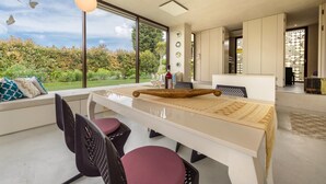 Un espace repas moderne avec une longue table, des chaises et une vue sur l’extérieur.