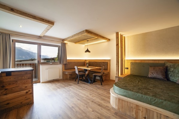 Une pièce avec un bureau en bois, un lit, une fenêtre donnant sur un beau paysage et un plafond avec des poutres apparentes.