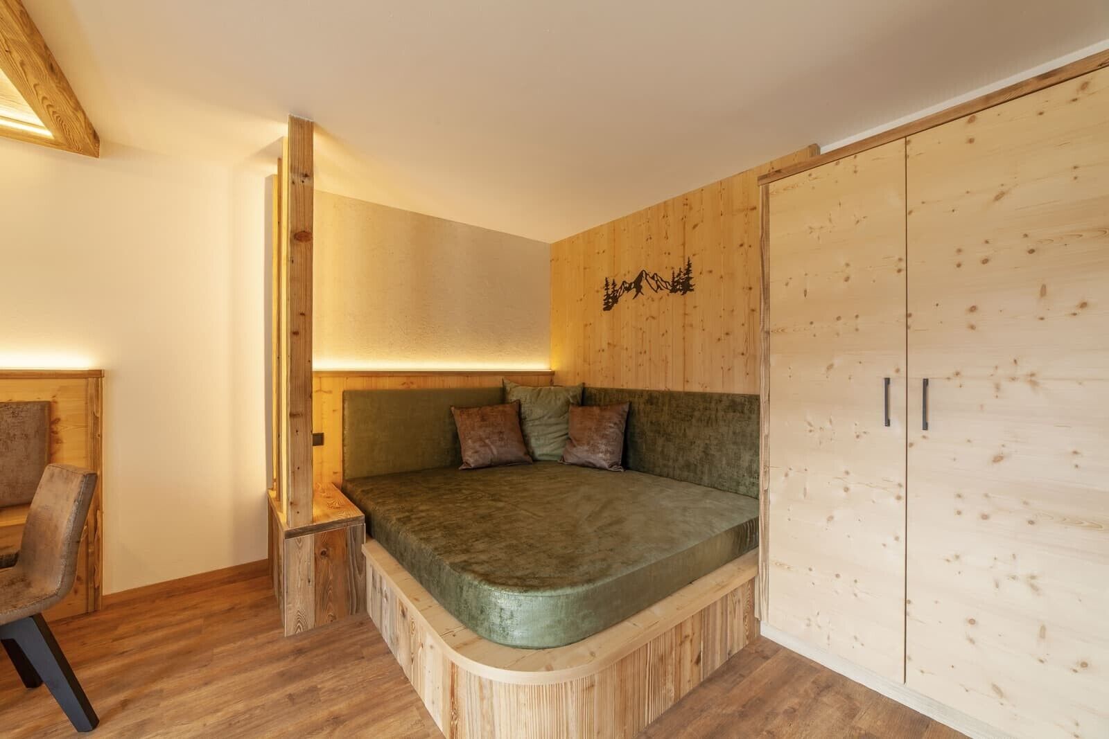 Un dormitorio con cama empotrada, paredes de madera, un armario de madera y una pequeña zona de estar.