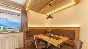 Un espace repas avec une table en bois, des bancs rembourrés, une suspension et une vue sur les montagnes par une fenêtre.